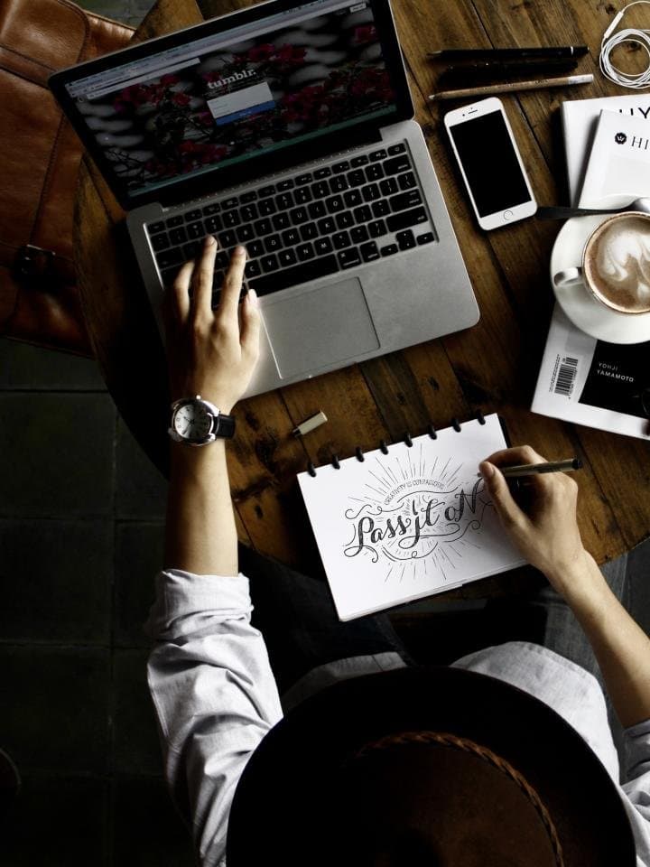 A desk seen from above with a laptop, a phone, a notebook and a coffee